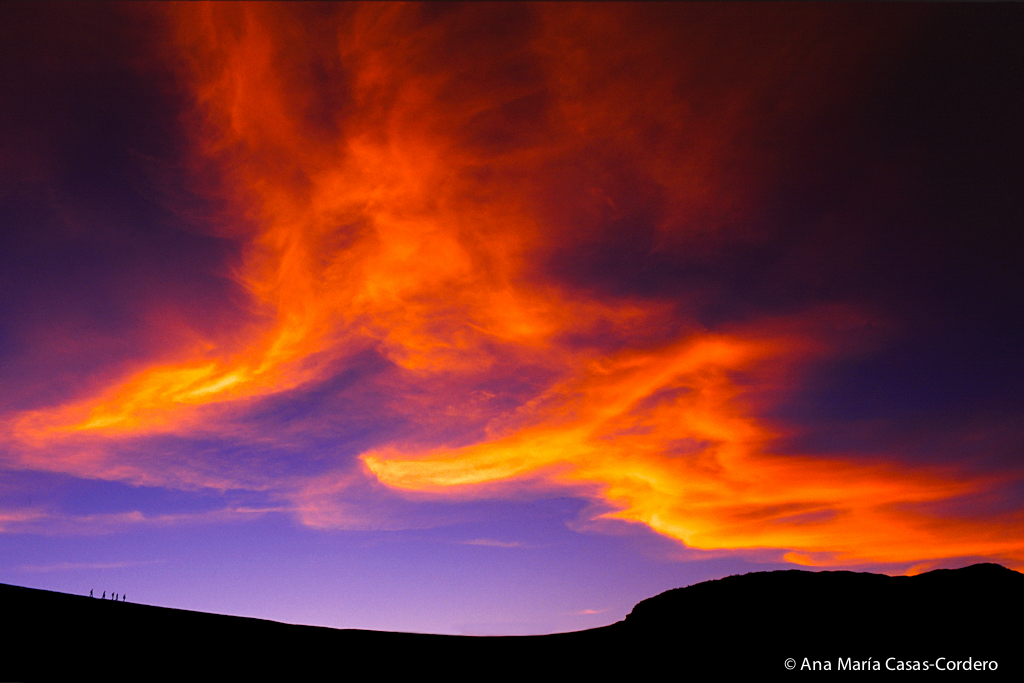 Fotografía de Paisaje de cielo con nubes encendidas y personas  en el horizonte caminando por el desierto